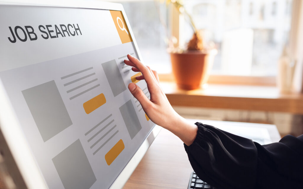 A hand using a touchscreen computer monitor with the words “job search” displayed on it.